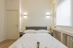 A hotel room with a bed, bedside tables, a window, and a radiator.