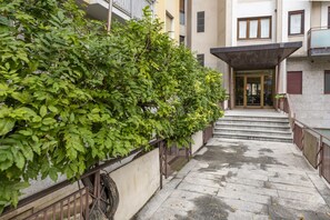A narrow stone pathway leading to a building entrance with a metal railing on one side and a green hedge on the other. - BnButler - Washington, 83 (Milano)