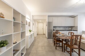 A modern kitchen with white cabinetry, a dining table with chairs, and a bookshelf with various items. - BnButler - Washington, 83 (Milano)