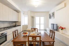 A modern kitchen with a dining area, a TV, and a window with curtains.