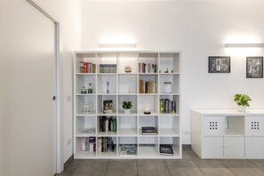 A white bookshelf with books and decorative items, a white cabinet with a plant, and framed pictures on the wall. - BnButler - Washington, 83 (Milano)