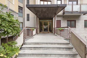 Entrada de un edificio con una escalera cubierta, una puerta de cristal y el número '88' sobre la puerta.