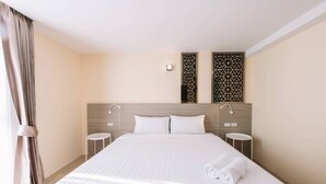 Habitació d'hotel amb un llit gran, dues taules de nit, un capçal de llit amb panells decoratius i una finestra amb cortines.