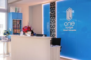 A reception desk with a blue wall featuring the 'one budget' logo and name. - One Budget Chiangrai Phahonyothin (Chiang Rai)