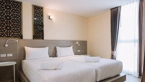Habitació d'hotel amb dos llits, una taula de nit, una làmpada penjada a la paret i un panell decoratiu.