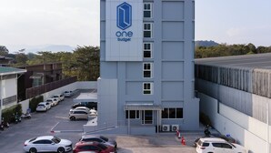 Un bâtiment moderne dont la façade est ornée du logo « un budget », un parking où sont garées plusieurs voitures et un ciel dégagé.