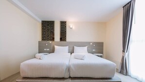 Un llit doble amb llençols blancs, dues tauletes de nit penjades a la paret i un panell decoratiu sobre el llit.