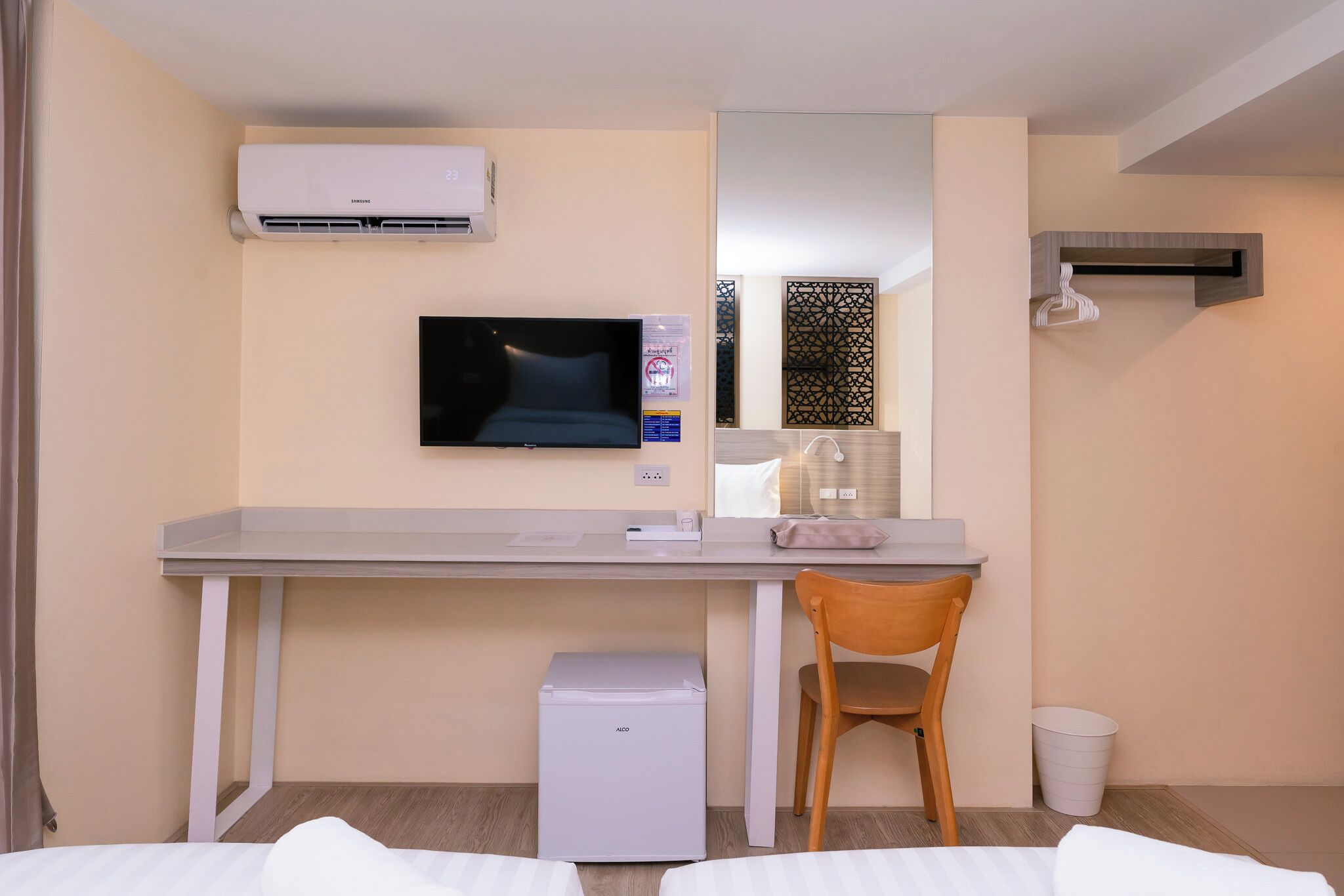 Habitación de hotel con cama, escritorio con silla, televisión, aire acondicionado, refrigerador pequeño y cesto de basura.