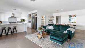 A modern living room with a green sofa, a coffee table, and a kitchen area with a refrigerator and stove. - Casa Cumpari in Wannanup (Wannanup)