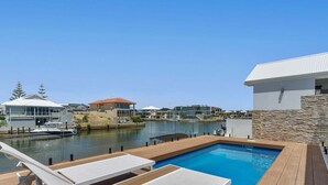 A pool area with lounge chairs, a view of the water, and buildings in the background. - Casa Cumpari in Wannanup (Wannanup)