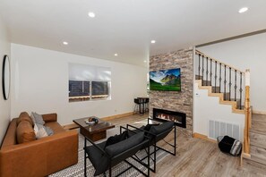 A modern living room with a fireplace, a sofa, a coffee table, and a staircase.