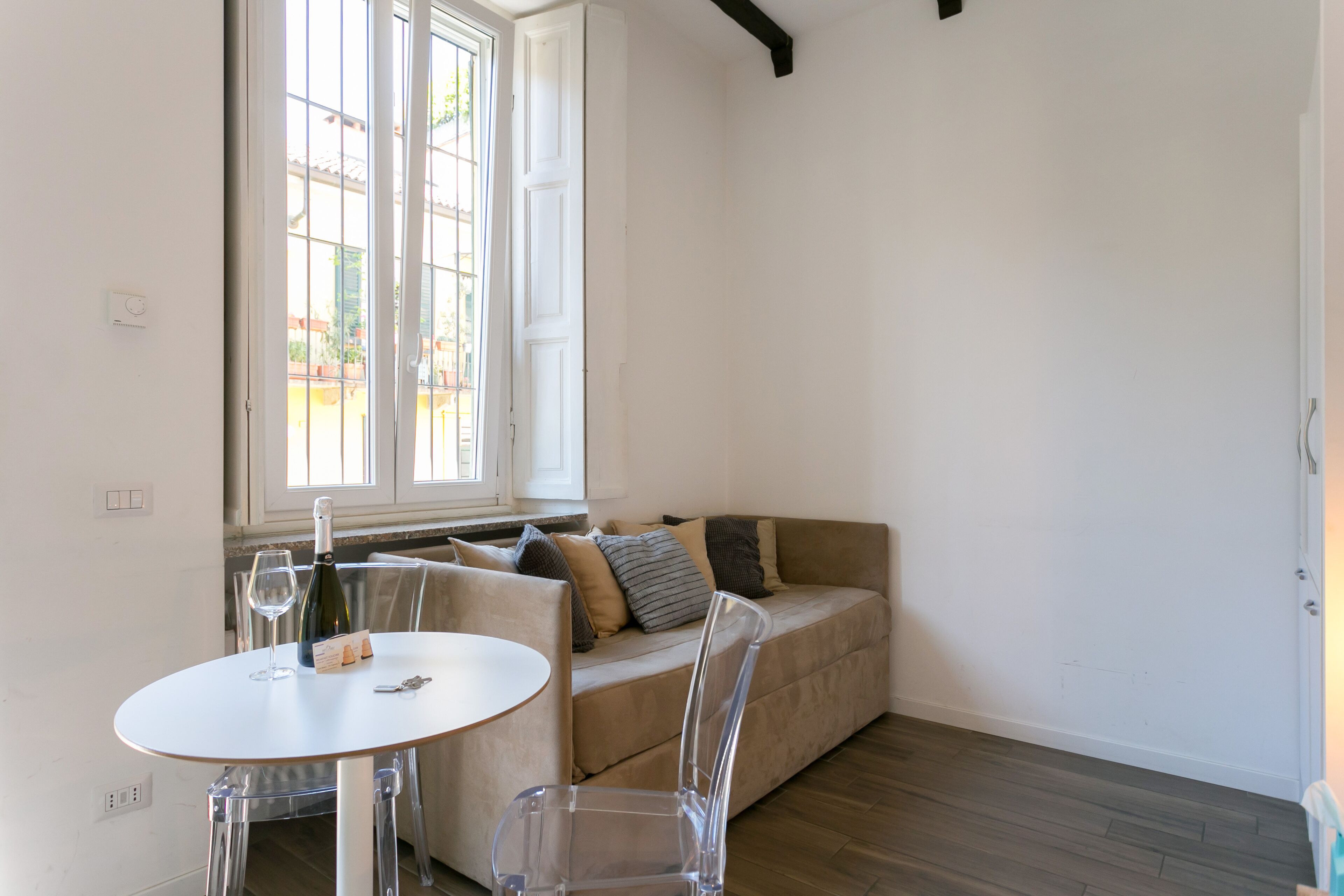 A room with a round table, a sofa, and a window with a view of the outside.