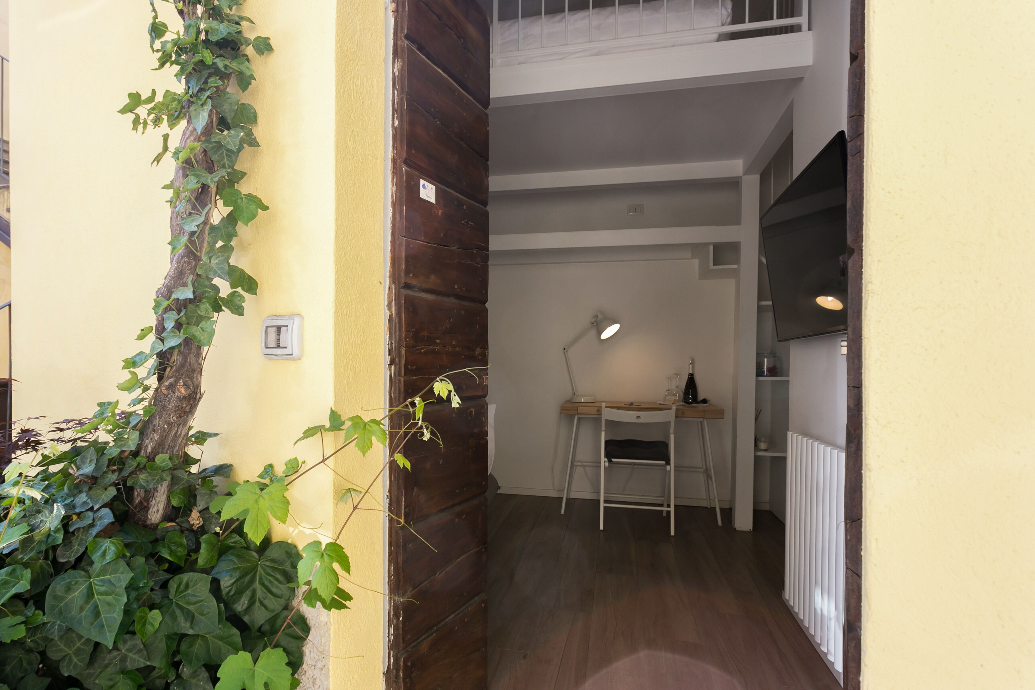 Un pasillo estrecho con una puerta de madera, un escritorio pequeño con una silla y un radiador.