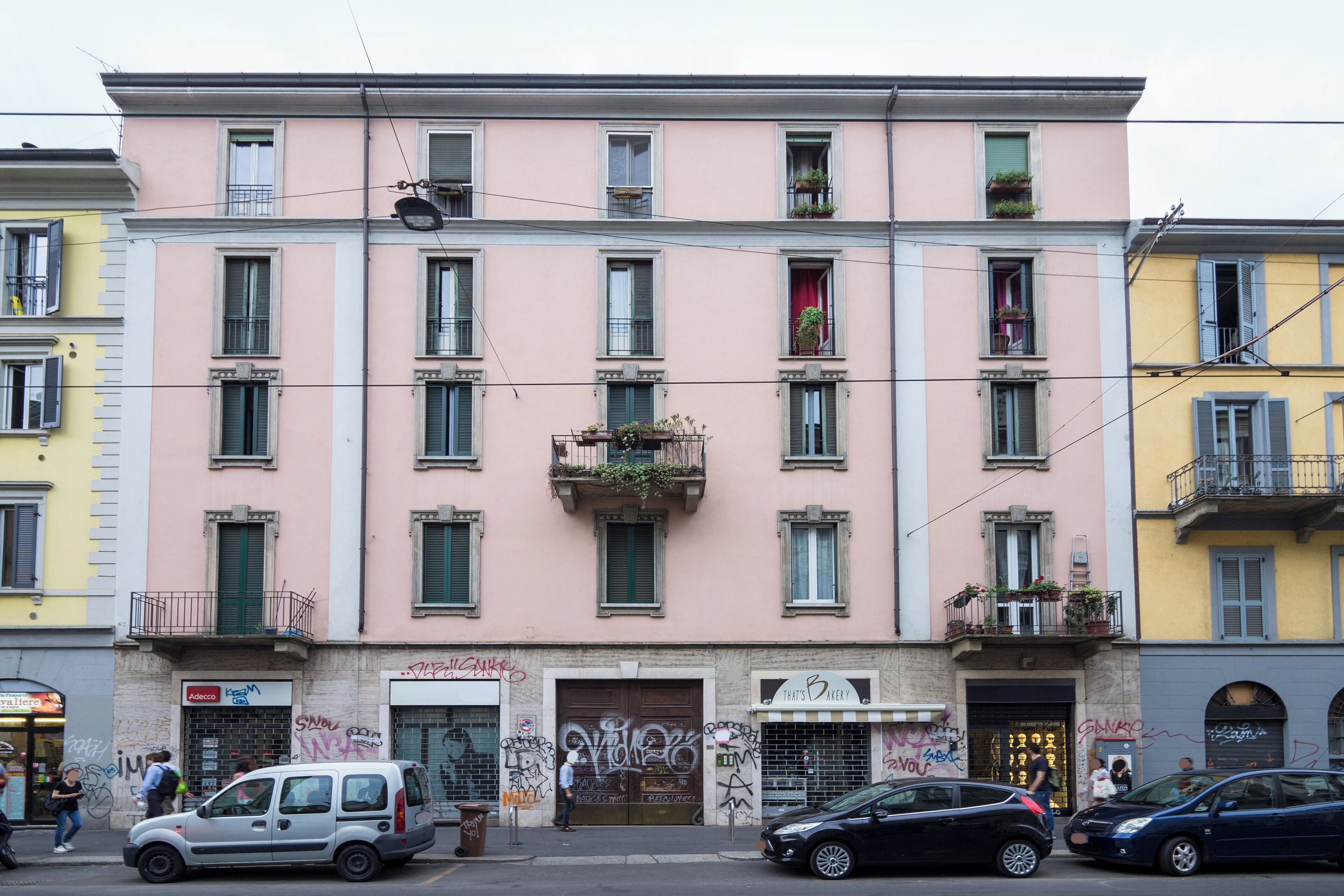 A multi-story building with balconies, a storefront, and parked cars.