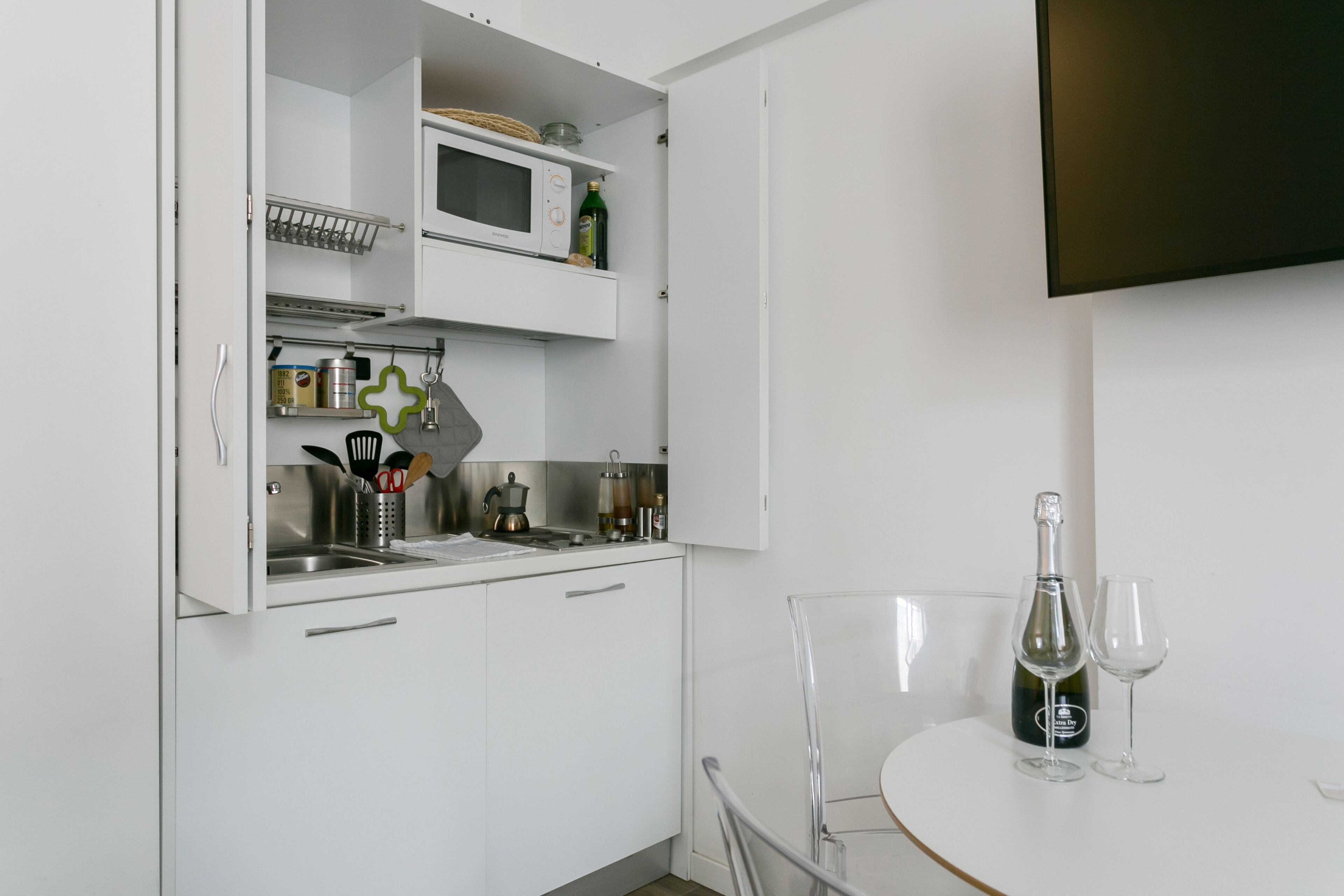 A modern kitchen with white cabinets, a microwave, and a wine bottle on a table.