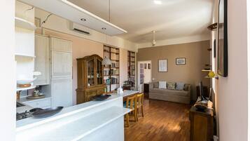 Una cocina moderna con armarios blancos, una mesa de comedor de madera y una zona de estar acogedora con sofá y televisor.