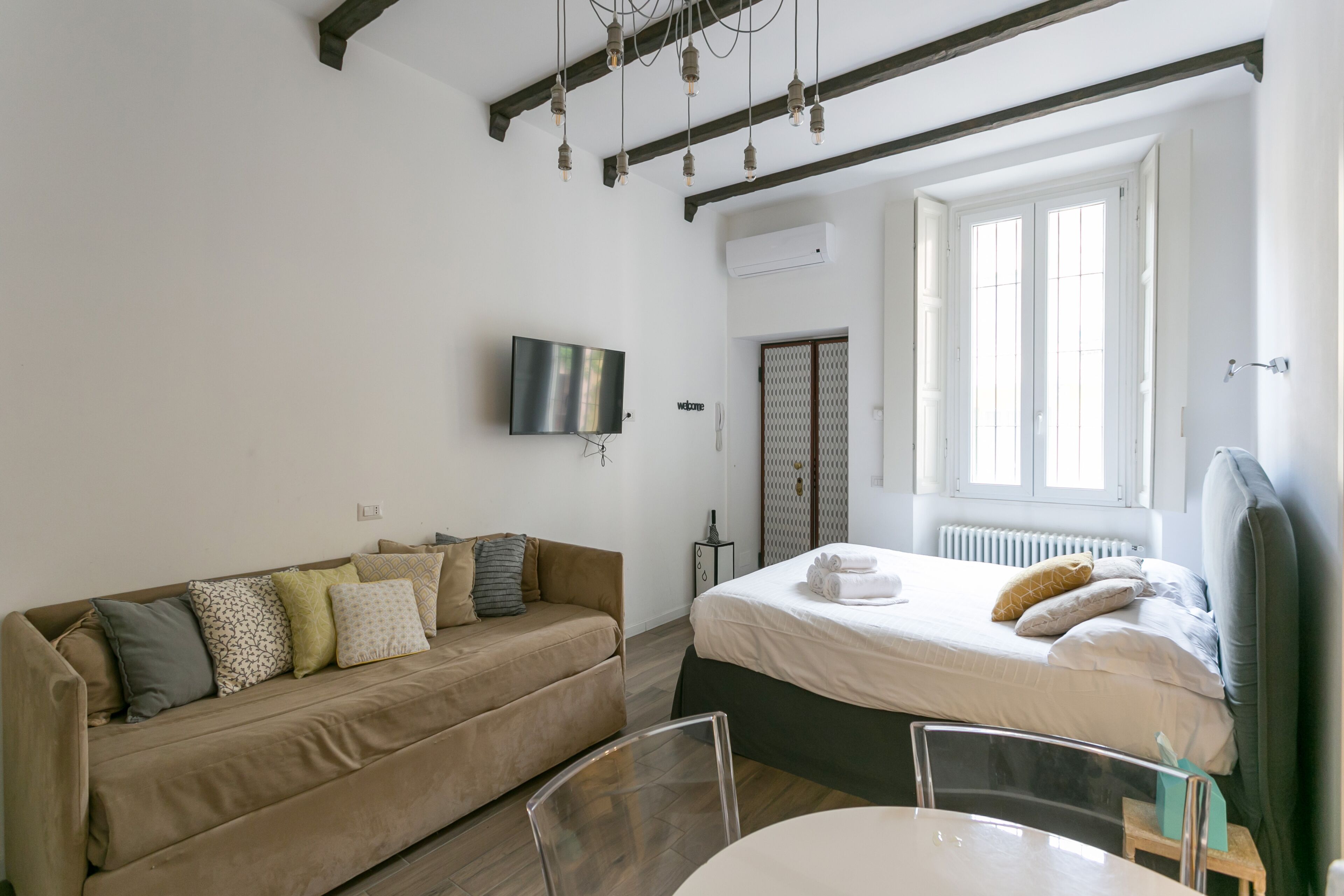 A modern bedroom with a bed, a sofa, a TV, and a window.