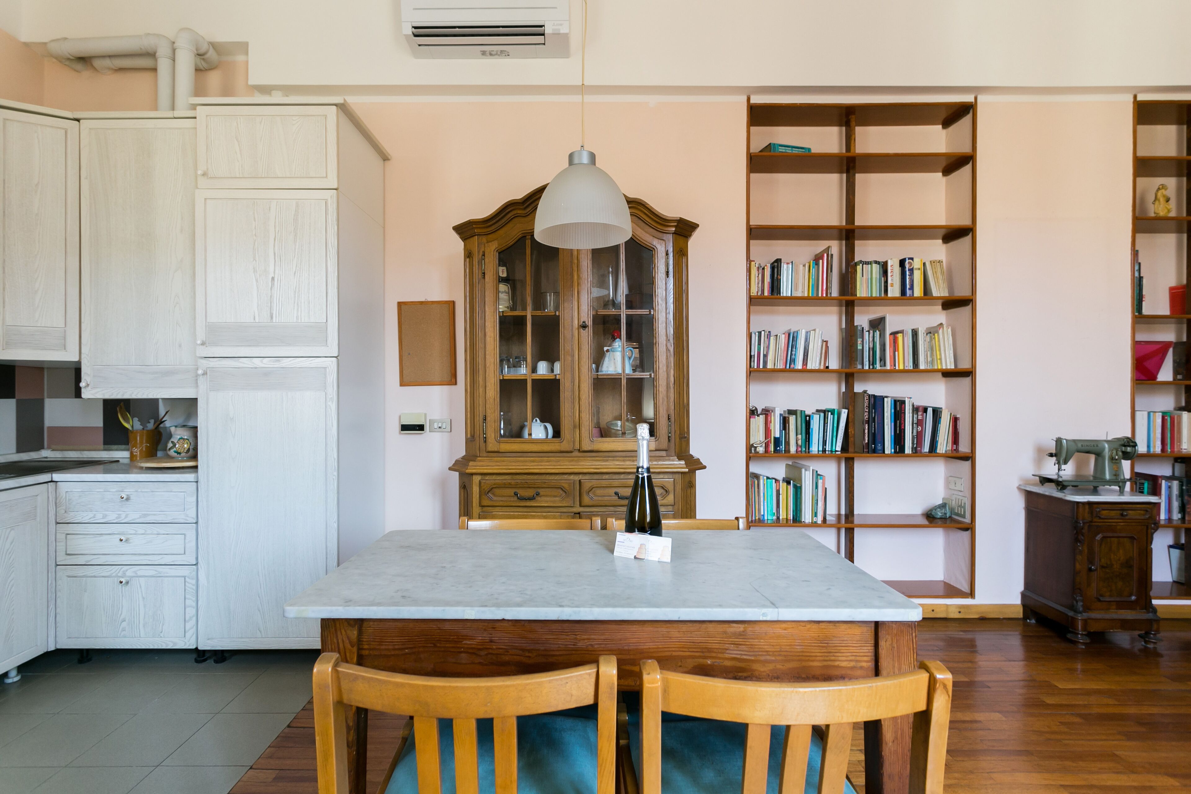 A dining area with a marble table, wooden chairs, a cabinet with glass doors, and a bookshelf filled with books.