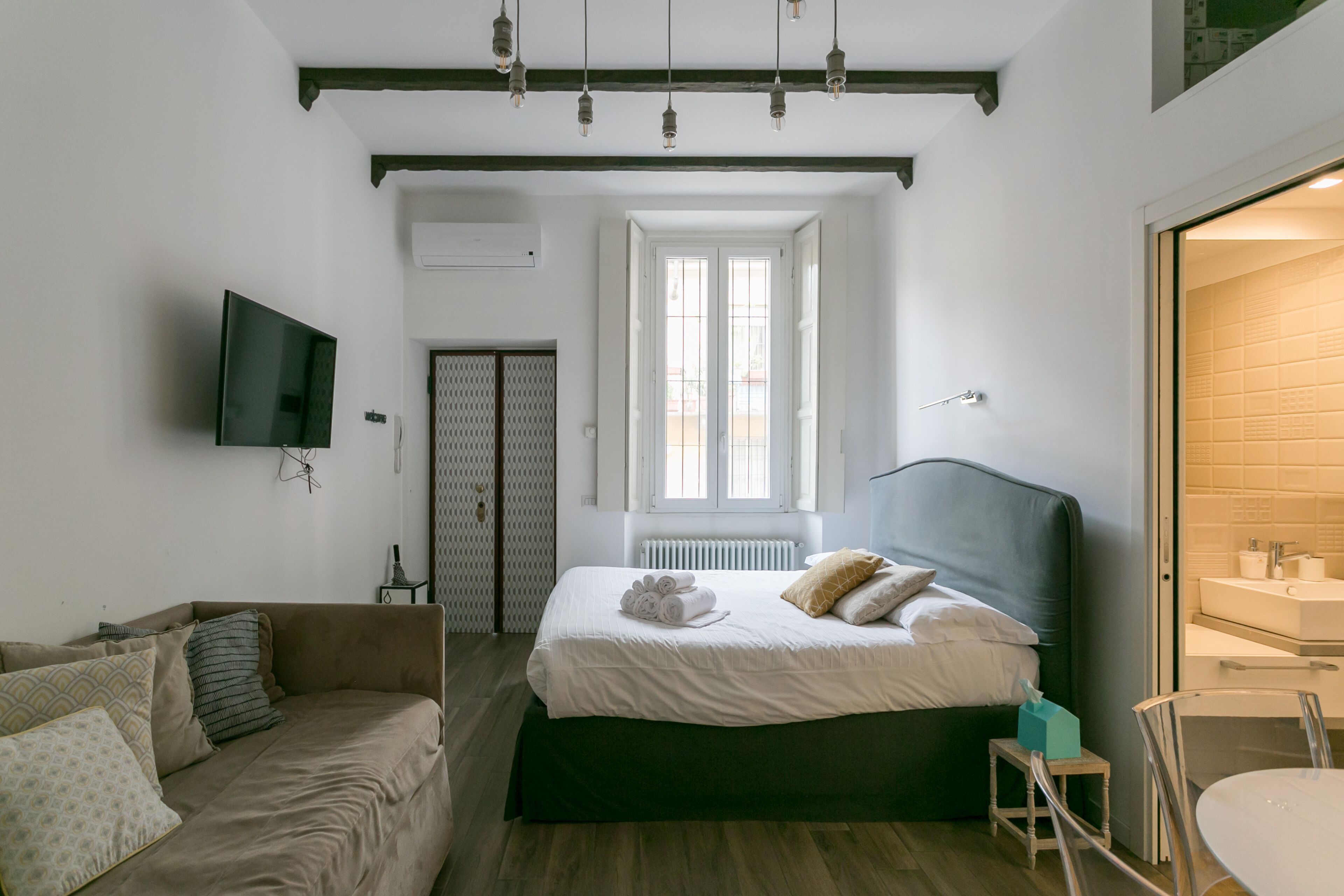 Una camera da letto con un letto, un divano, una TV e un bagno visibile attraverso una porta aperta.