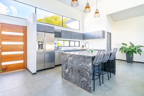 Une cuisine moderne dotée d’un îlot en marbre, d’appareils électroménagers en acier inoxydable et d’une grande fenêtre.