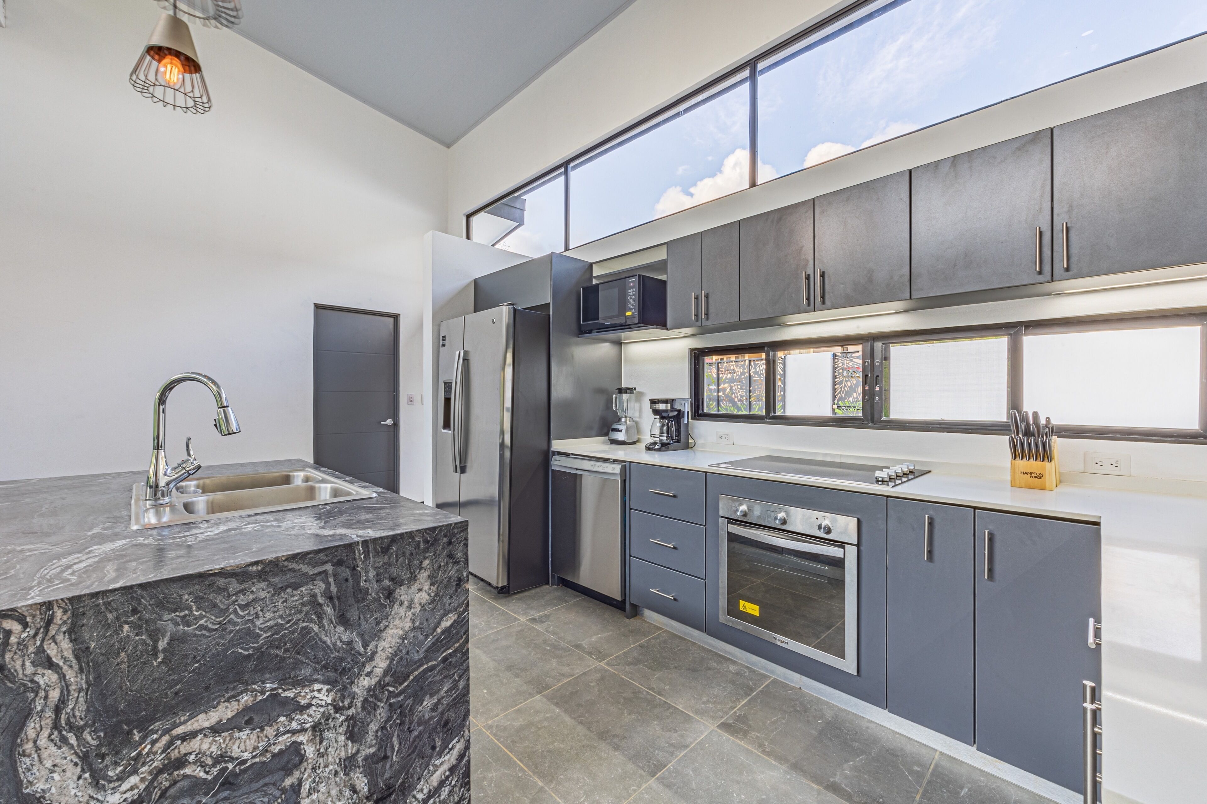 A modern kitchen with a marble island, stainless steel appliances, and a large window providing natural light.