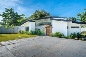 Une maison moderne avec une allée en béton, une porte d’entrée en bois et une pelouse bien entretenue.