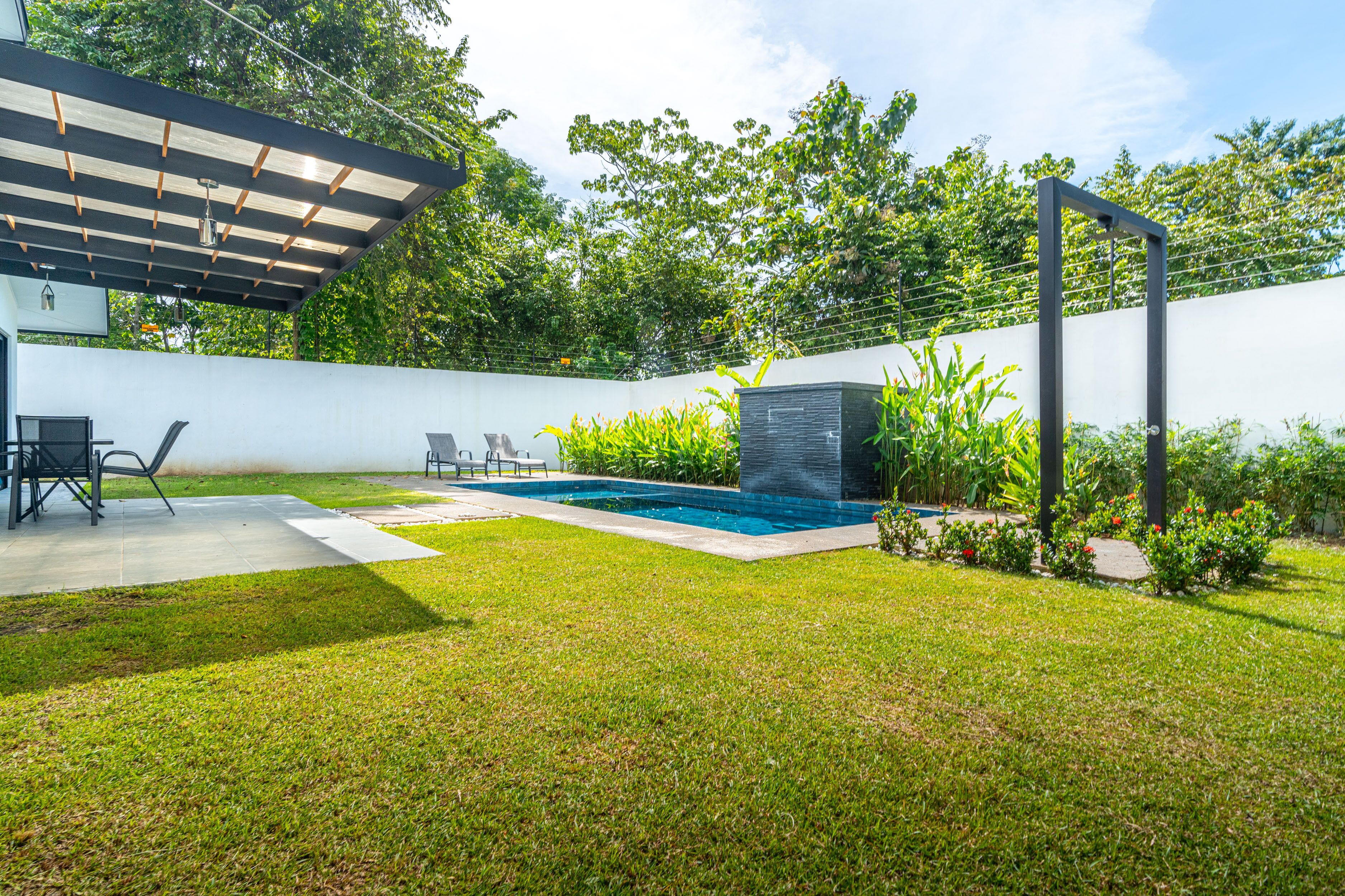 Un jardin avec une piscine, une pergola et un espace détente avec des chaises.