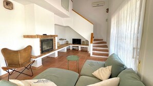 Un salon comprenant un canapé, un fauteuil, une cheminée, un téléviseur et un escalier.