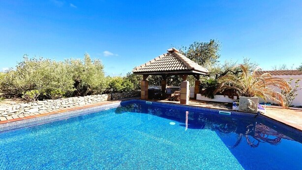 Une piscine d’un bleu éclatant, bordée d’une terrasse carrelée, entourée de verdure et agrémentée d’un belvédère.