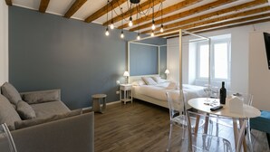 Een moderne slaapkamer met een bed, nachtkastjes, een ronde eettafel met stoelen en een groot raam.