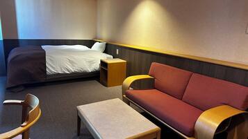 Une chambre d’hôtel avec un lit, un canapé rouge, une table en bois et un fauteuil en bois.