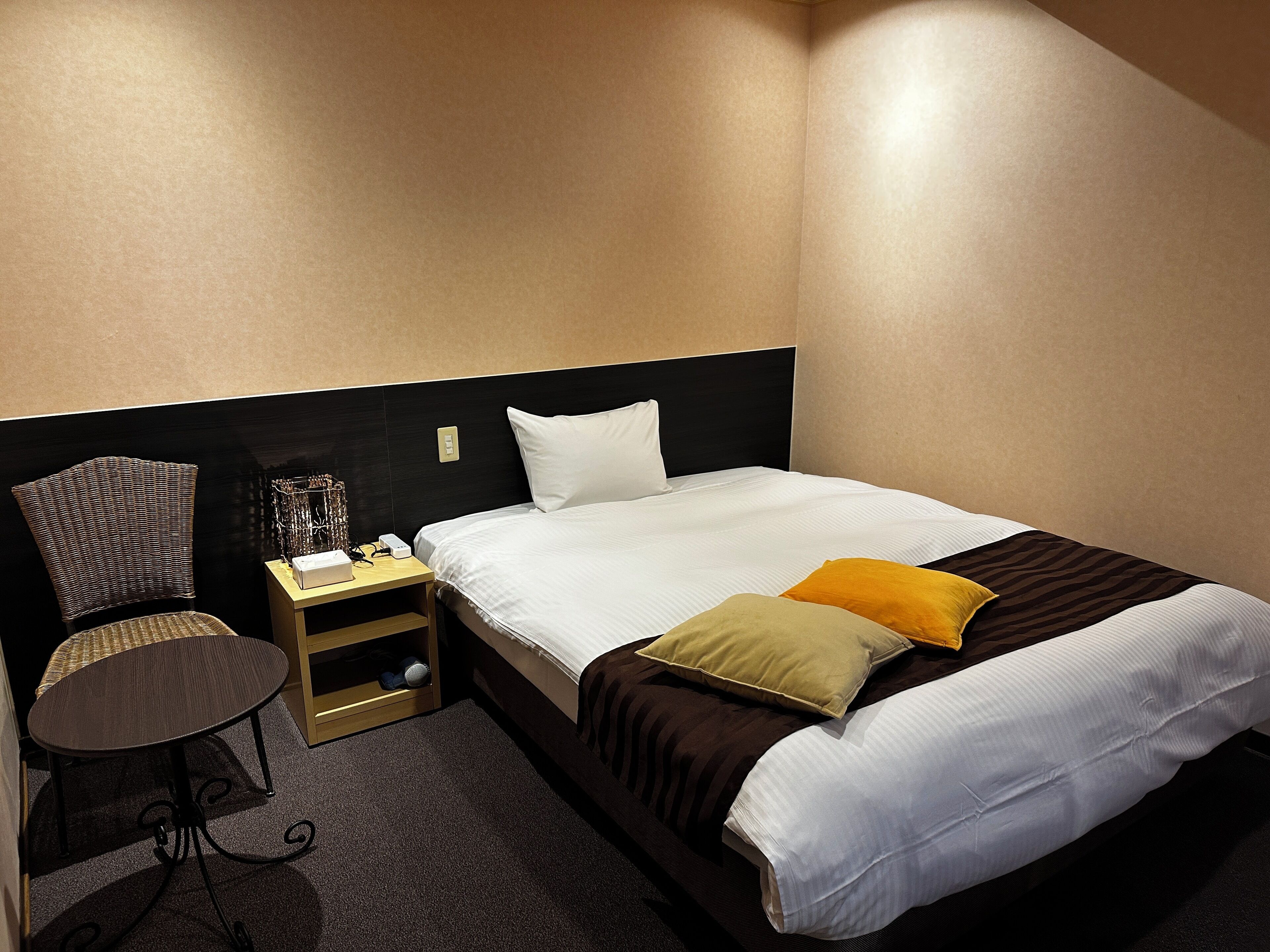 Una habitación de hotel con cama, una silla, una mesita de noche y una lámpara.