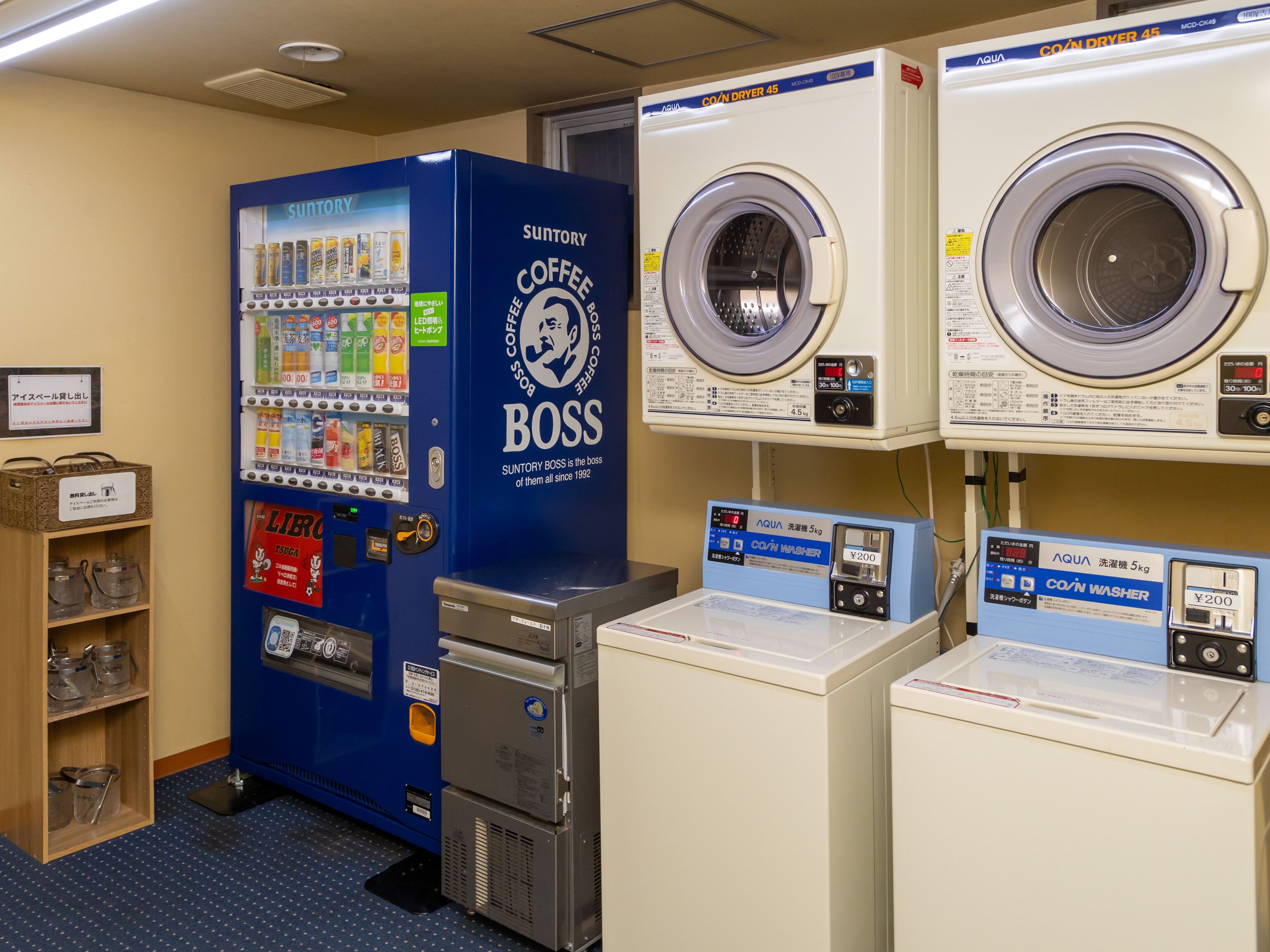 A laundromat with a Suntory Coffee Boss vending machine, two washing machines, and a coin-operated washer.