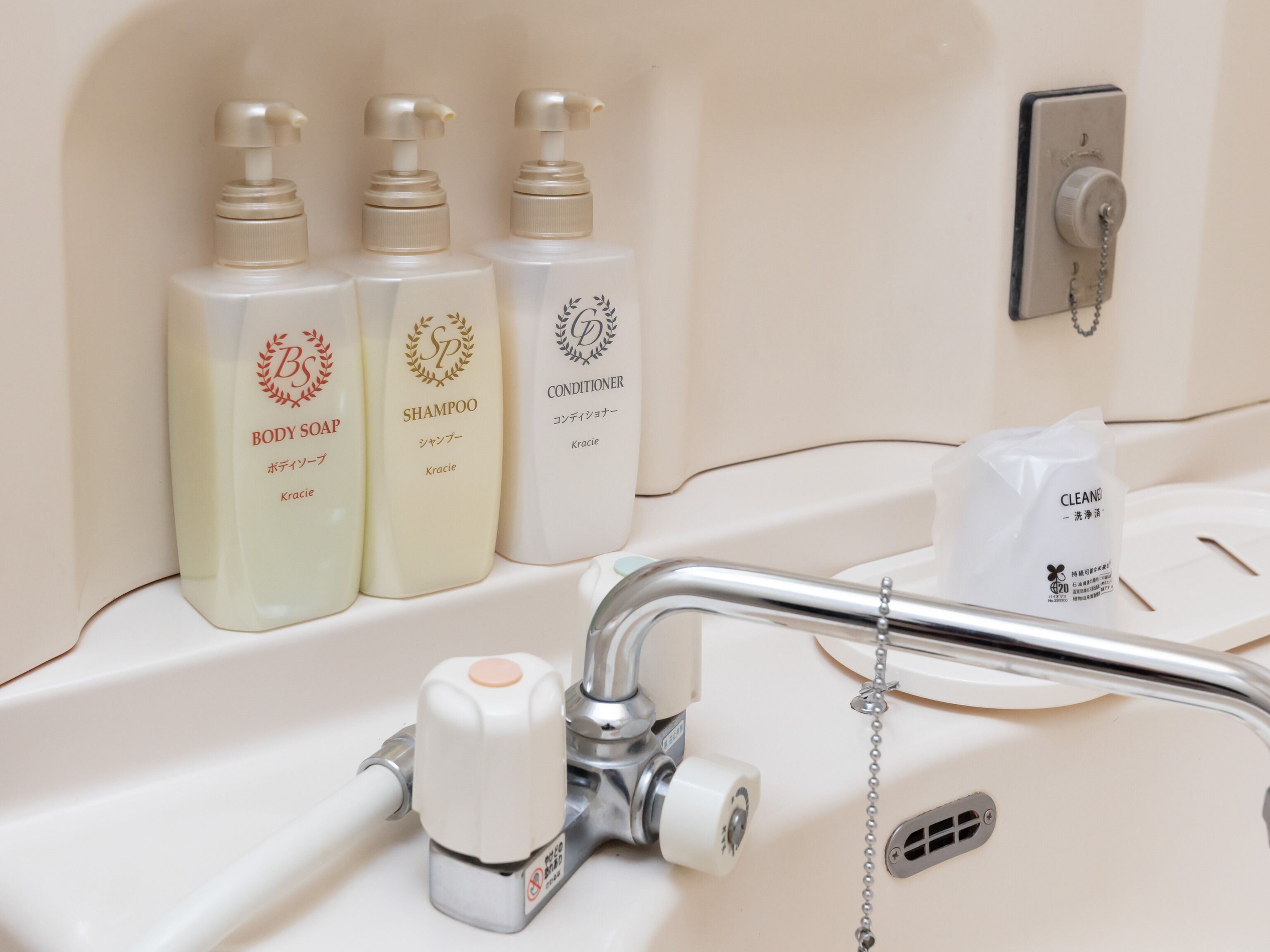 A bathroom sink with three bottles of body soap, shampoo, and conditioner.