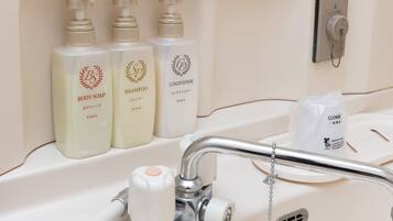 A bathroom sink with three bottles of body soap, shampoo, and conditioner.