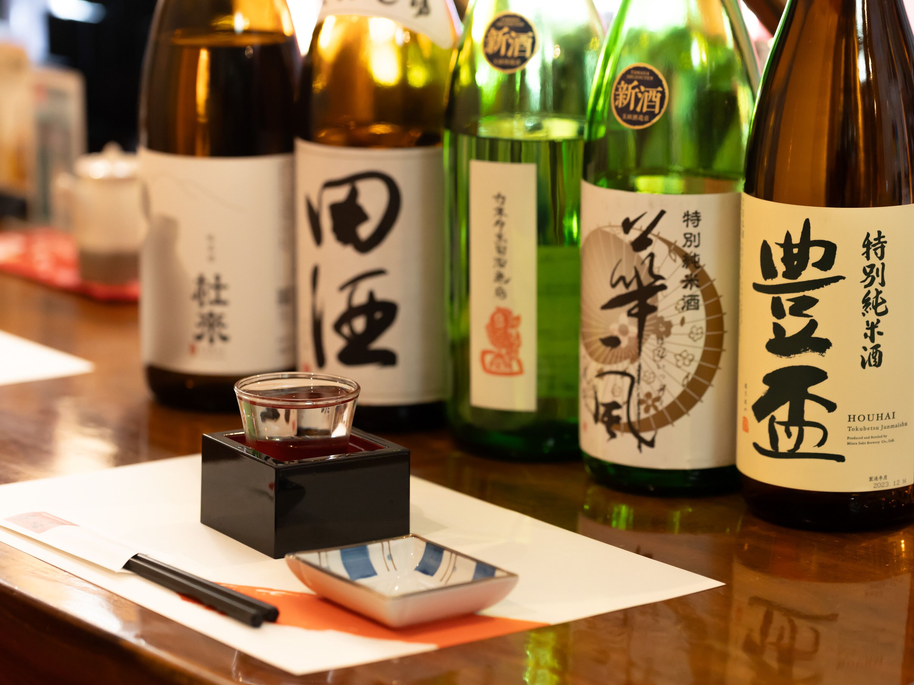 A selection of sake bottles on a table with a small dish of soy sauce and chopsticks.