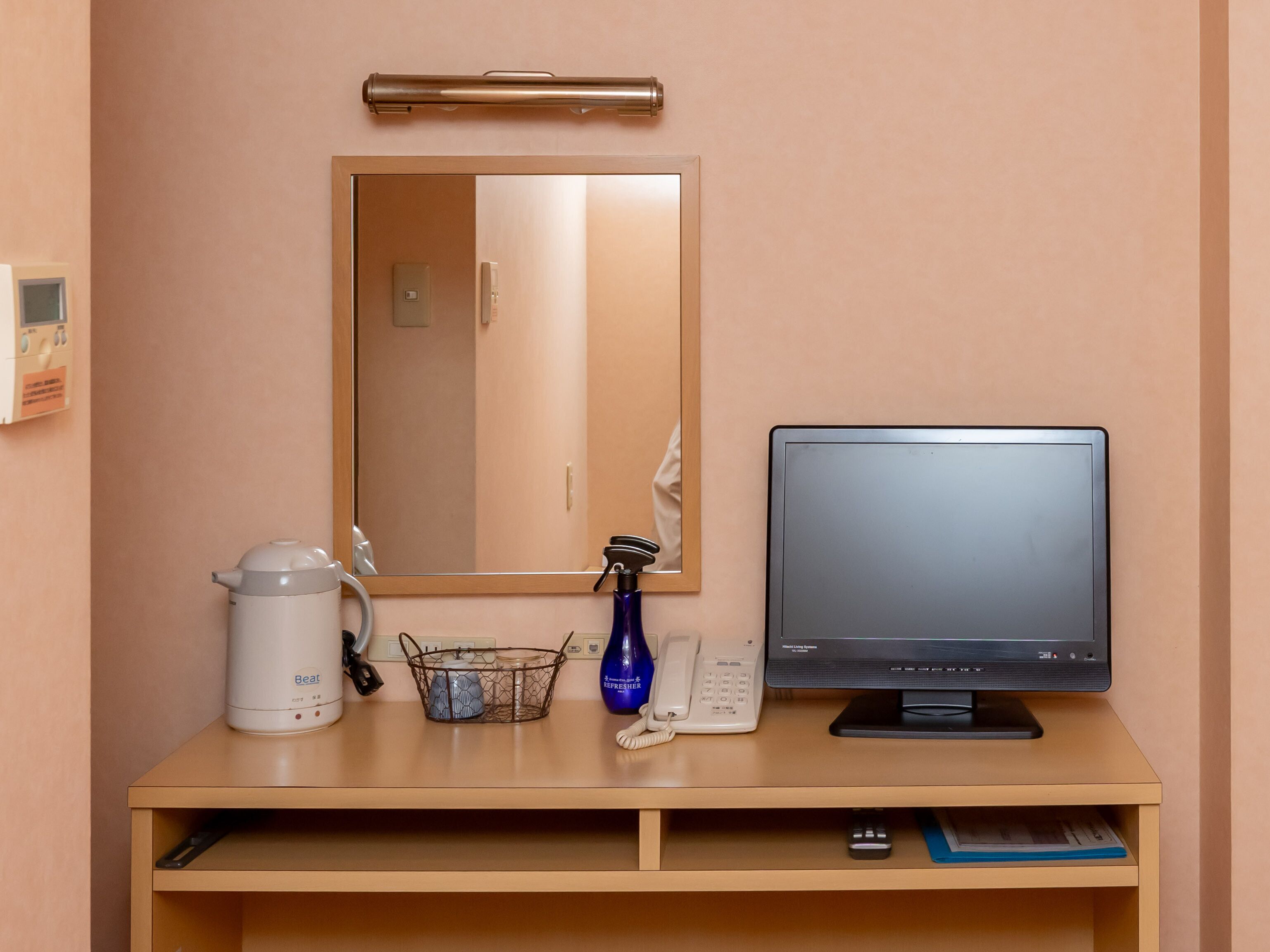 A hotel room with a wooden desk, a flat-screen TV, a kettle, a blue vase, a telephone, and a mirror.