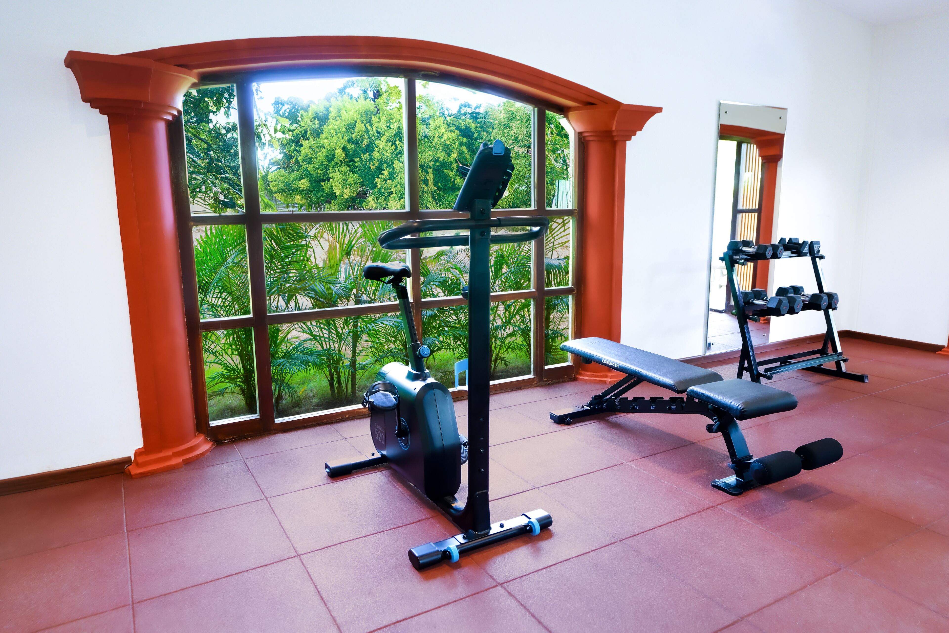A gym with exercise equipment, large windows, and a bench.