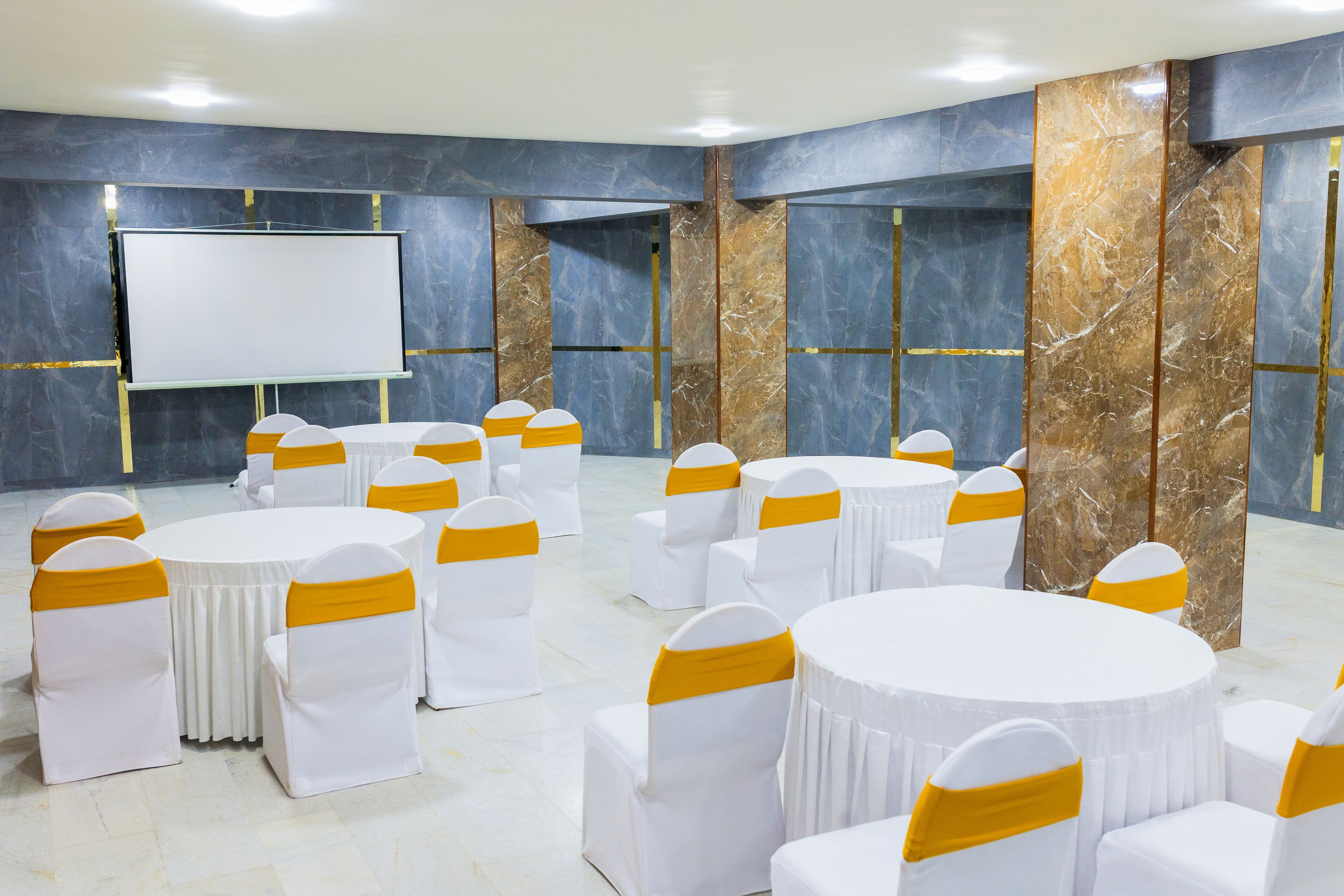A conference room with white tables and chairs, a large screen, and marble walls.