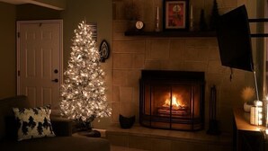 A cozy living room with a lit fireplace, a Christmas tree, and a comfortable sofa.
