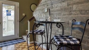 A dining area with a table and two chairs, a wooden wall, and a door leading outside.