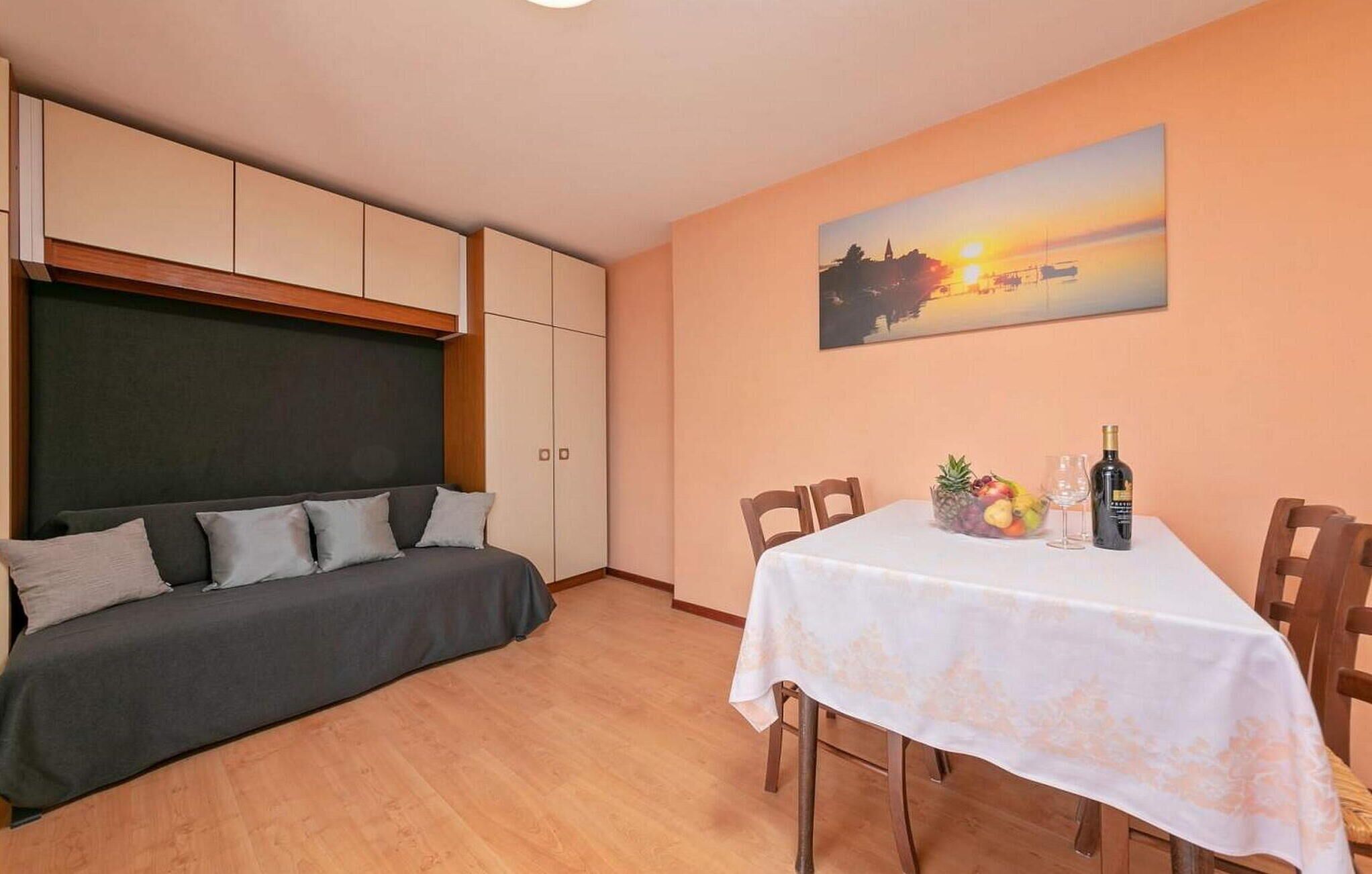 Une pièce comprenant un lit, une table à manger avec des chaises et un tableau représentant un coucher de soleil.
