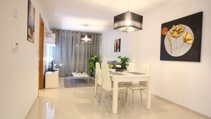 Un comedor moderno con una mesa y sillas blancas, una lámpara colgante y un cuadro de flores en la pared.