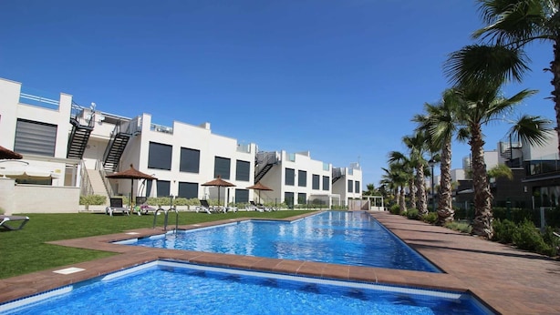 Ein Swimmingpool mit klarem, blauem Wasser, umgeben von Palmen und einem modernen Gebäude mit Balkonen.