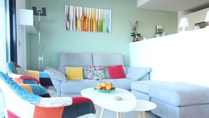 Ein modernes Wohnzimmer mit einem grauen Sofa, bunten Kissen, einem weißen Couchtisch und einer Obstschale.