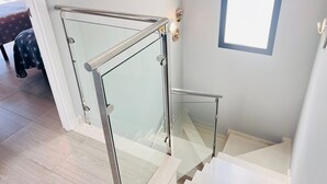 Un escalier avec des rampes en verre et une main courante, menant à un palier doté d’une porte.