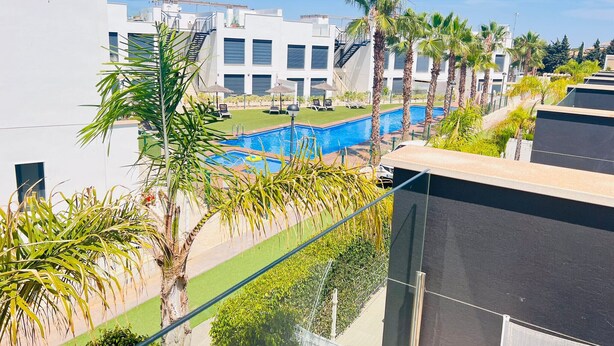 Un bâtiment moderne doté d’une piscine sur le toit, entouré de palmiers et surplombant un ciel d’un bleu limpide.