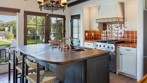 A kitchen with a large island, a stove, and a sink. There are wicker chairs around the island.