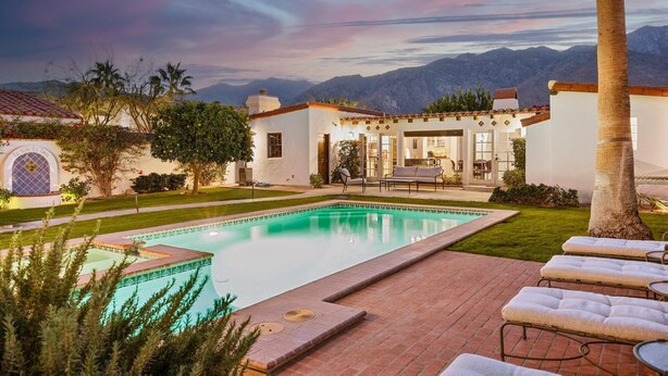 A pool area with a patio, lounge chairs, and a view of mountains.