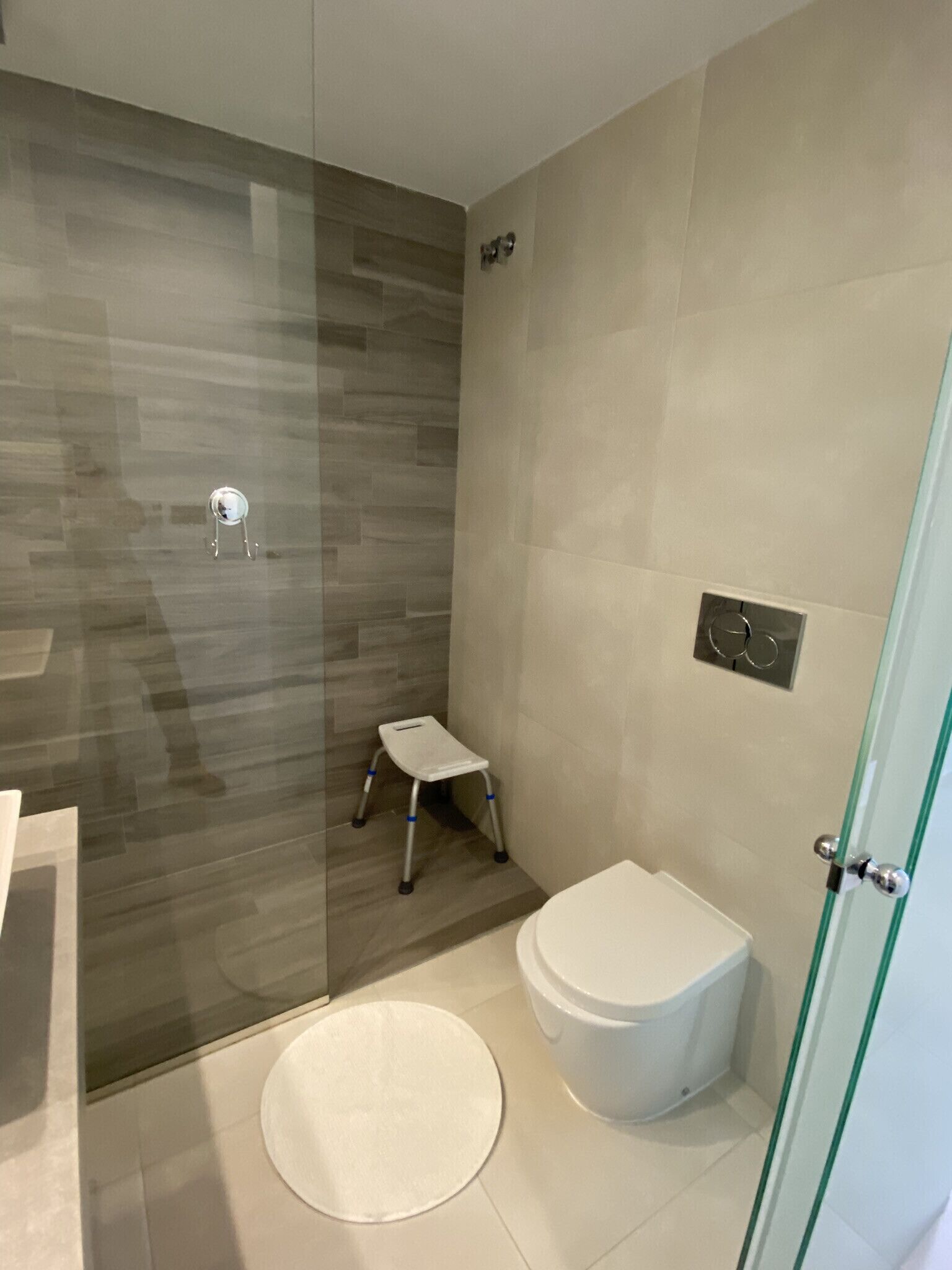 Een moderne badkamer met een douchecabine van glas, een wit toilet en een klein opstapkrukje.